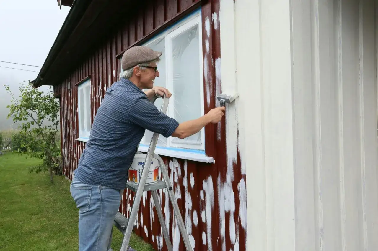 Man p&aring; stege m&aring;lar huset vitt. F&ouml;nstret &auml;r t&auml;ckt med plast.