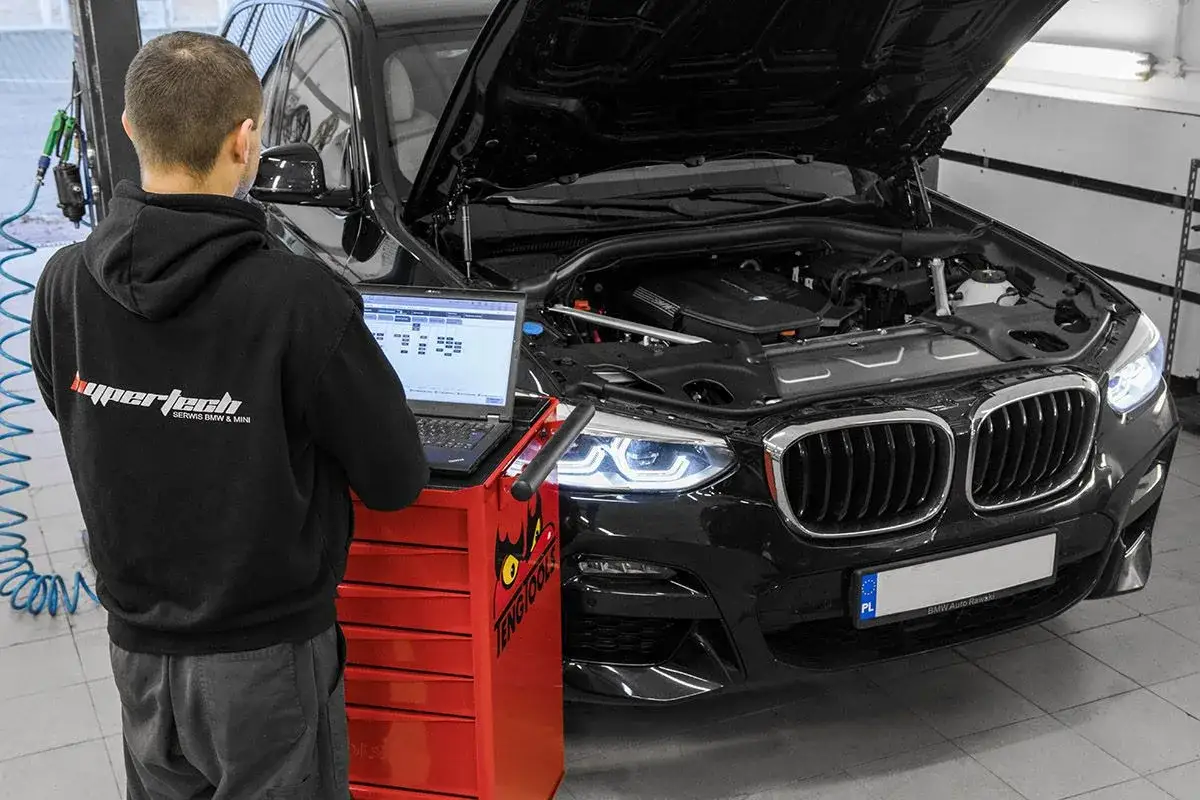 Mechanik diagnozuje check engine w BMW, używając laptopa.