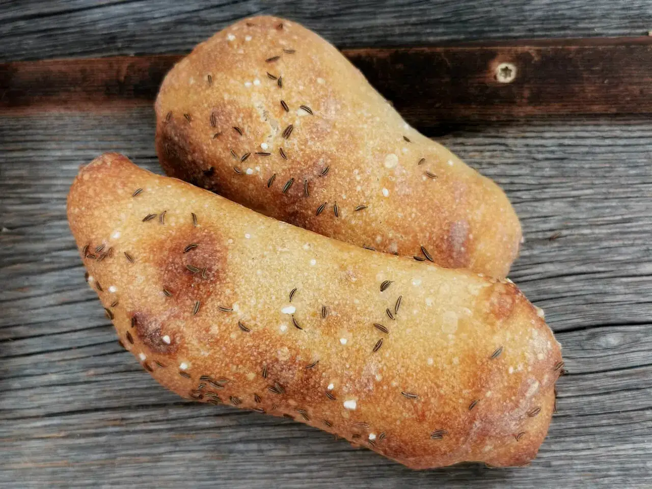 Zwei goldbraune Kümmelbrötchen liegen auf rustikalem Holz. Perfekt, um die Seele zu essen.