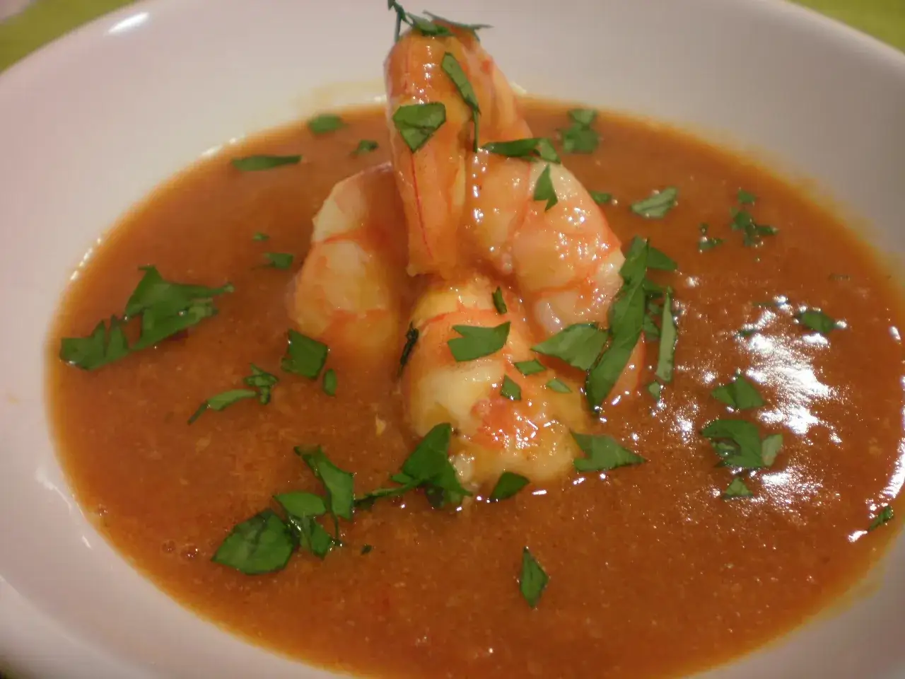 Un cremoso bisque de langosta, adornado con gambas y perejil fresco picado, servido en un cuenco blanco.