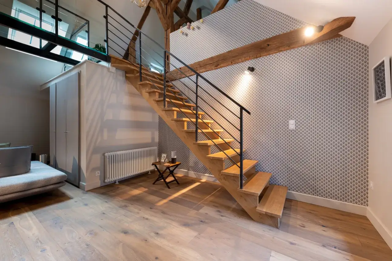 Escalier en bois avec rambarde noire, un escalier claustra moderne dans un loft aux poutres apparentes et papier peint graphique.