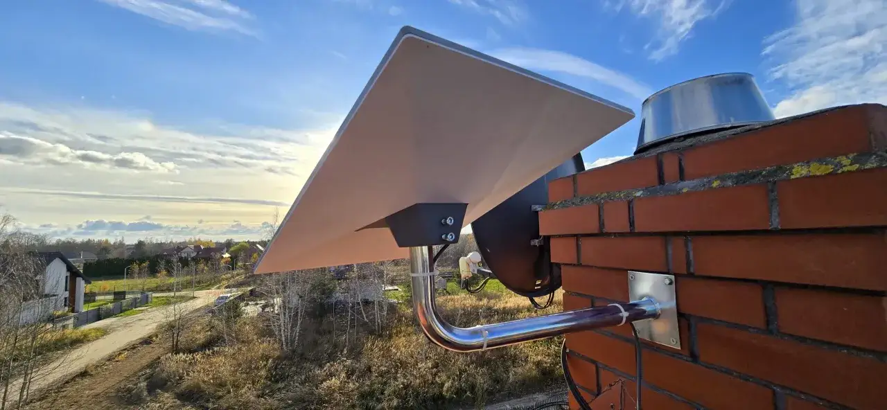 Antena Starlink zamontowana na kominie, gotowa do zapewnienia szybkiego internetu. W tle domy i błękitne niebo.