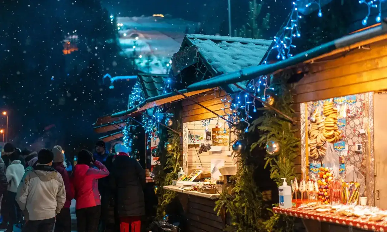 Atmosfera magica nei mercatini di Natale nelle Marche, con bancarelle illuminate da luci blu e addobbi natalizi, mentre la neve cade dolcemente.
