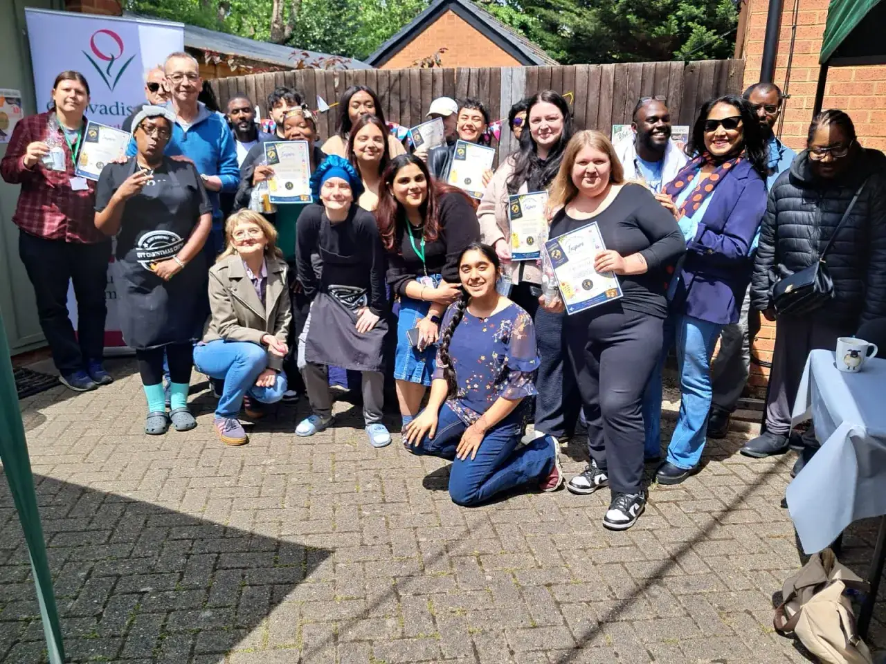 A diverse group of people, many holding certificates, pose for a photo outdoors. Thank you for your service to the community.