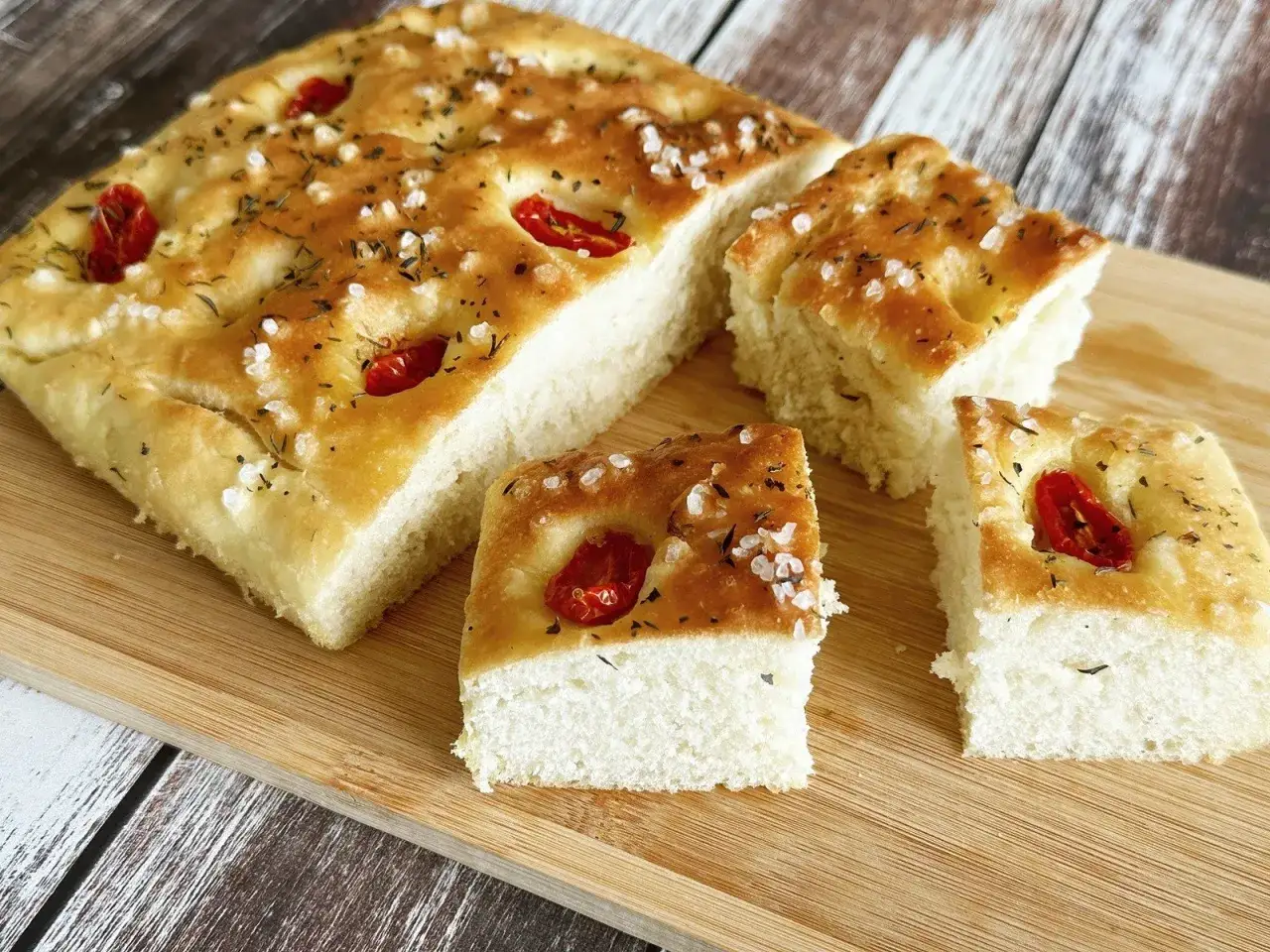 Oryginalna włoska focaccia przepis: puszyste ciasto z pomidorkami koktajlowymi, ziołami i solą morską, pokrojone na kawałki.