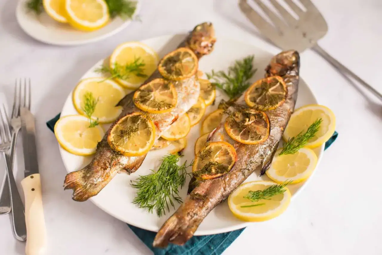 Tv&aring; hela ugnsbakade regnb&aring;gar med citronskivor och dill p&aring; en vit tallrik.
