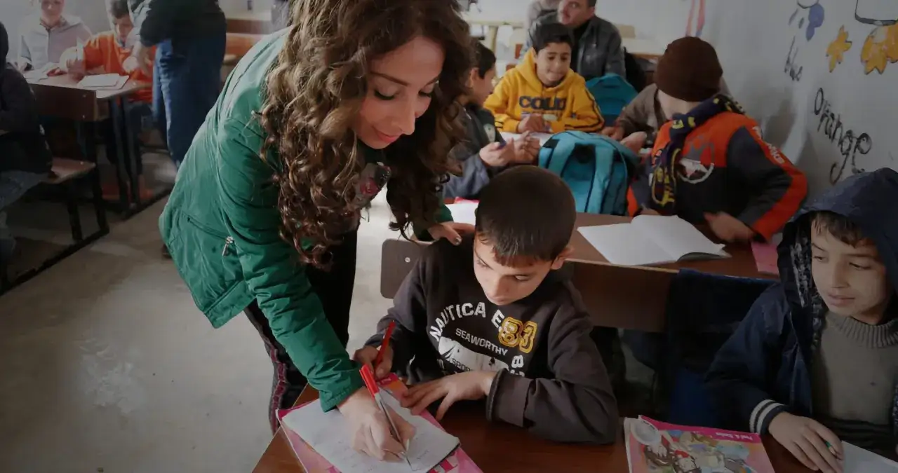 Insegnante aiuta un bambino con disabilità a scrivere. La classe è piena di bambini che studiano.