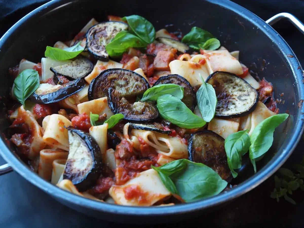 Herzhafte Pasta Melanzane mit gebratenen Auberginenscheiben und frischem Basilikum in einer Pfanne.