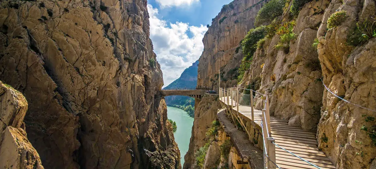 En dramatisk vy över Caminito del Rey i Málaga, med gångvägar längs klippväggar och en bro över en turkos flod.