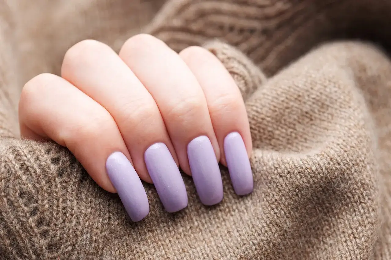 Dłoń z paznokciami w kolorze lawendowym, idealny przykład, co to jest manicure hybrydowy.