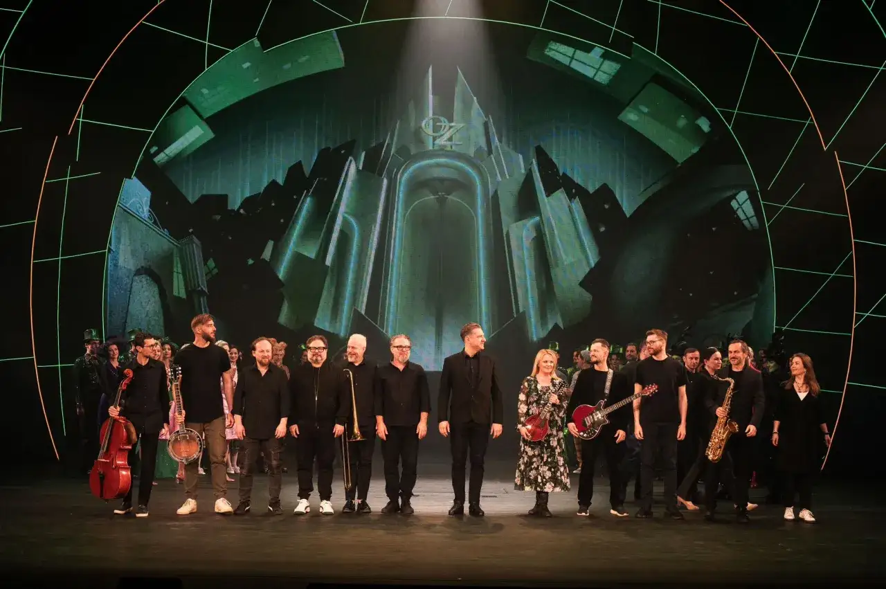 Zespół muzyczny i obsada na scenie przed ekranem z napisem