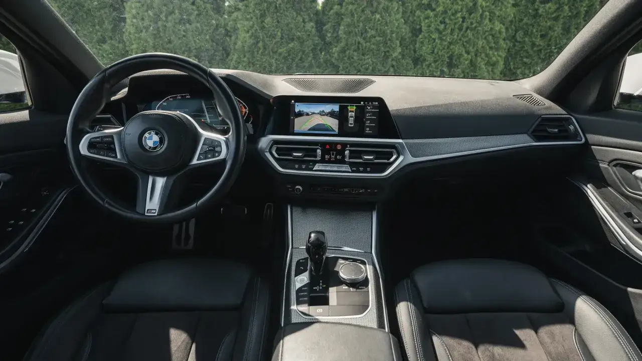 Wnętrze BMW 318d: kierownica, ekran multimedialny z widokiem z kamery cofania, dźwignia zmiany biegów i czarne fotele.