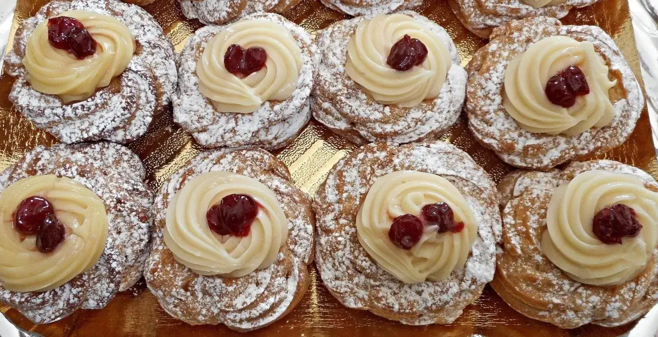 Zeppole, dolci tipici della Basilicata, ricoperte di zucchero a velo e guarnite con crema pasticcera e amarene.