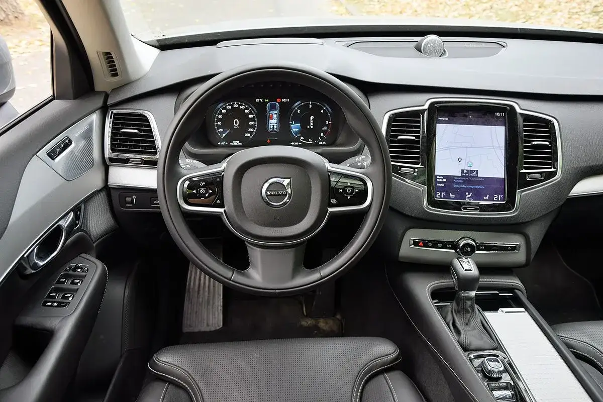 Wnętrze Volvo CX90 z ekranem nawigacji, cyfrowymi zegarami i skórzaną tapicerką.