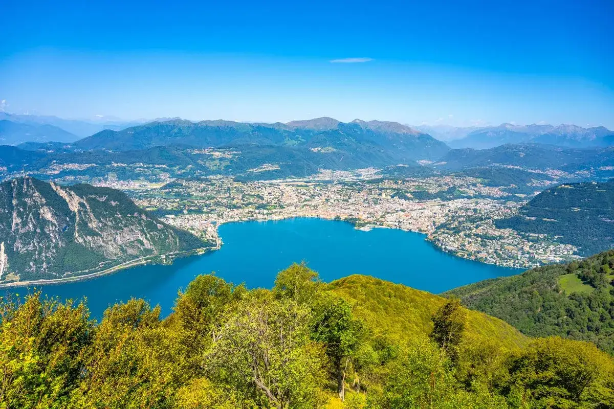 Vista panoramica di un lago blu intenso con una città costiera e montagne sullo sfondo. Sembra il balcone d'Italia.