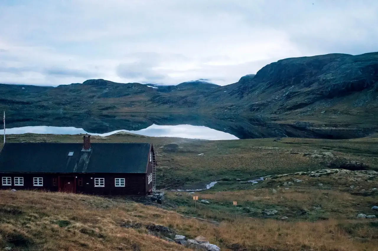 Ein einsames Haus am See, bereit f&uuml;r das n&auml;chste Abenteuer beim **Hardangervidda wandern**. Berge spiegeln sich im ruhigen Wasser.
