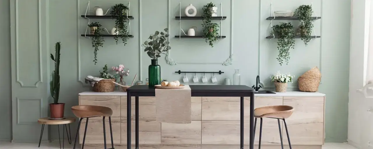Cucina moderna con pareti verde salvia, piante, mensole e un'isola centrale con sgabelli in pelle.