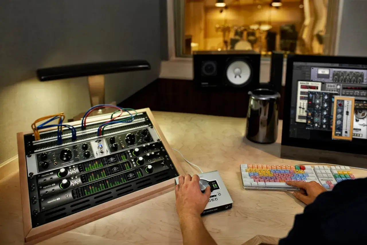 Hand bedient ein Audio-Interface, während ein **midi sequencer** auf dem Bildschirm zu sehen ist. Studio-Equipment und ein Schlagzeug im Hintergrund.