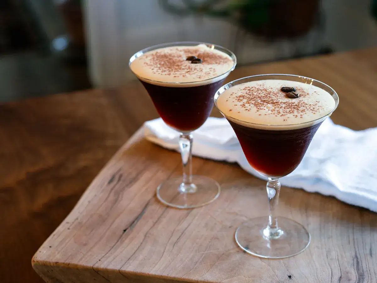 Deux verres de cocktail du moment, orn&eacute;s de grains de caf&eacute; et de cacao, sur une planche en bois.