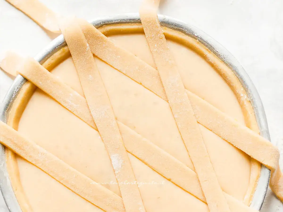 La pasta frolla per pastiera, tagliata a strisce, decora la crema in una tortiera.