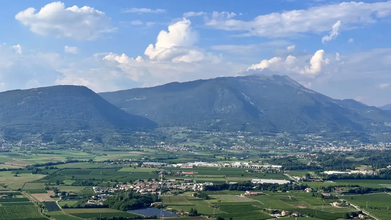 Panoramica di un paesaggio collinare con vigneti e montagne sullo sfondo. Affi cosa vedere: un borgo tra verdi colline e cime maestose.