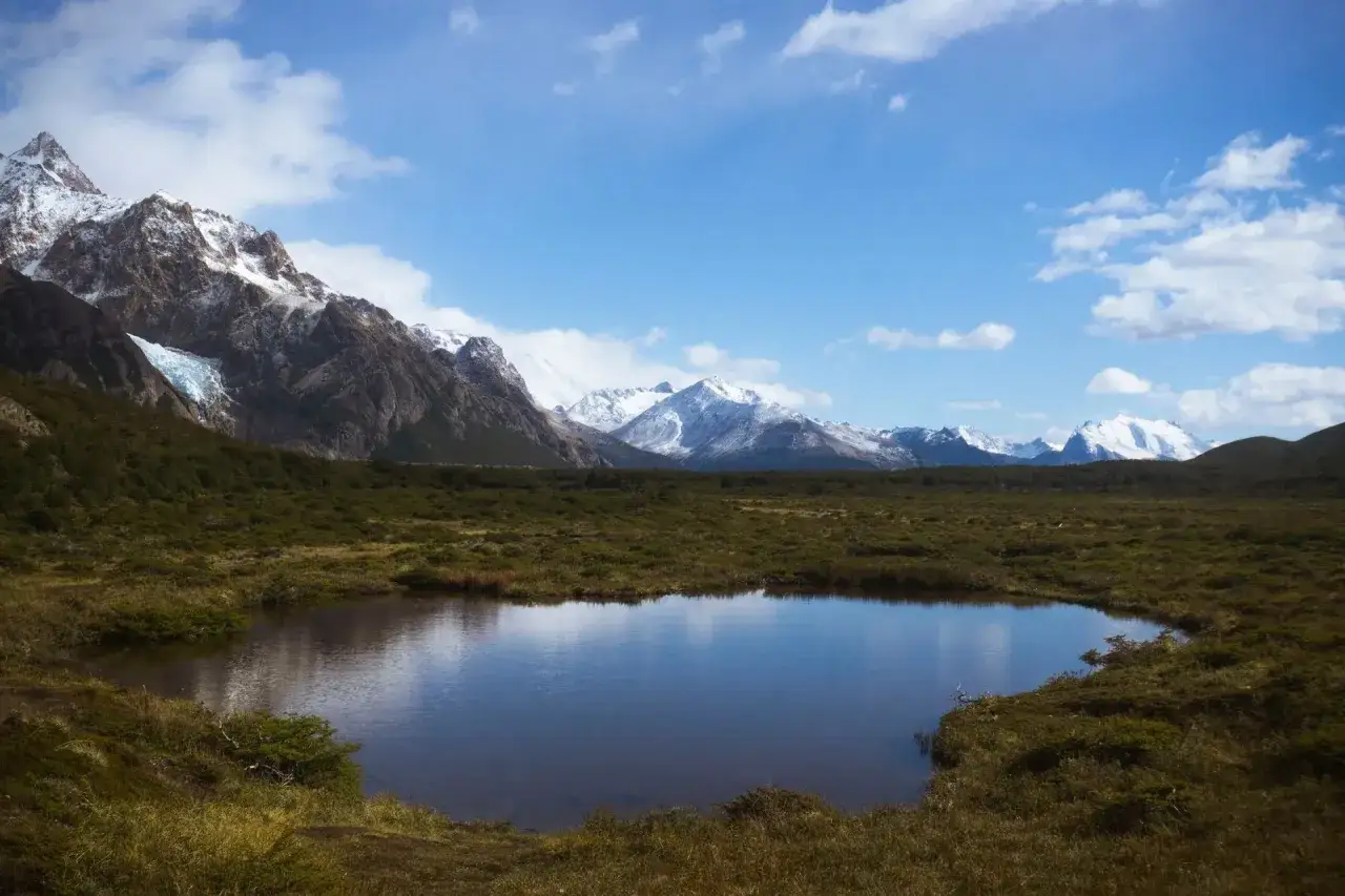 Spokojne jezioro odbija ośnieżone g&oacute;ry, w tym majestatyczne g&oacute;ry z Aconcagua, otoczone zielonymi wzg&oacute;rzami.