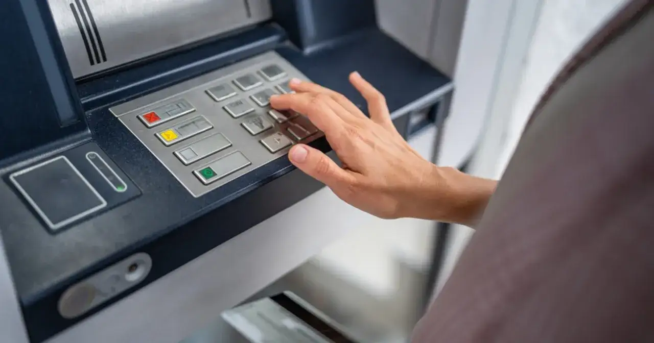 Dłoń wpisuje PIN na klawiaturze bankomatu, przygotowując się do transakcji, jak zmienić pin do karty.