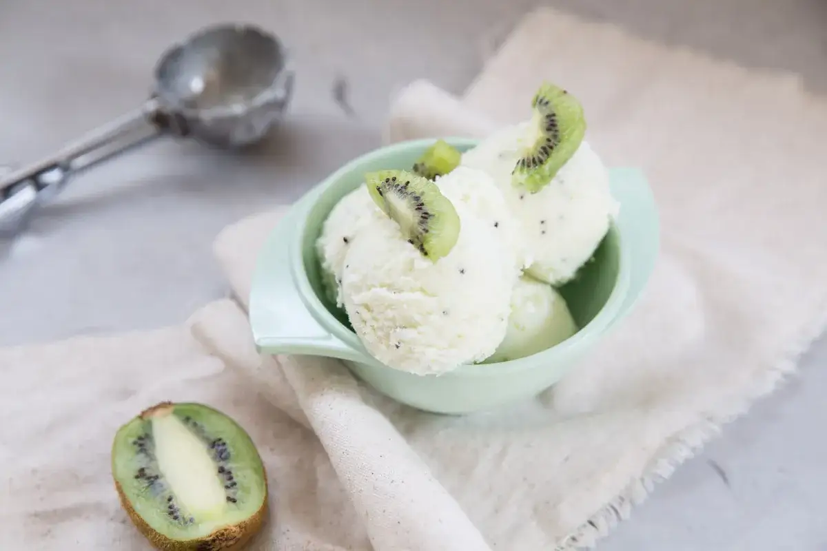 Sch&uuml;ssel mit erfrischendem Kiwi-Sorbet, garniert mit frischen Kiwischeiben. Daneben eine halbierte Kiwi und ein Eisportionierer.