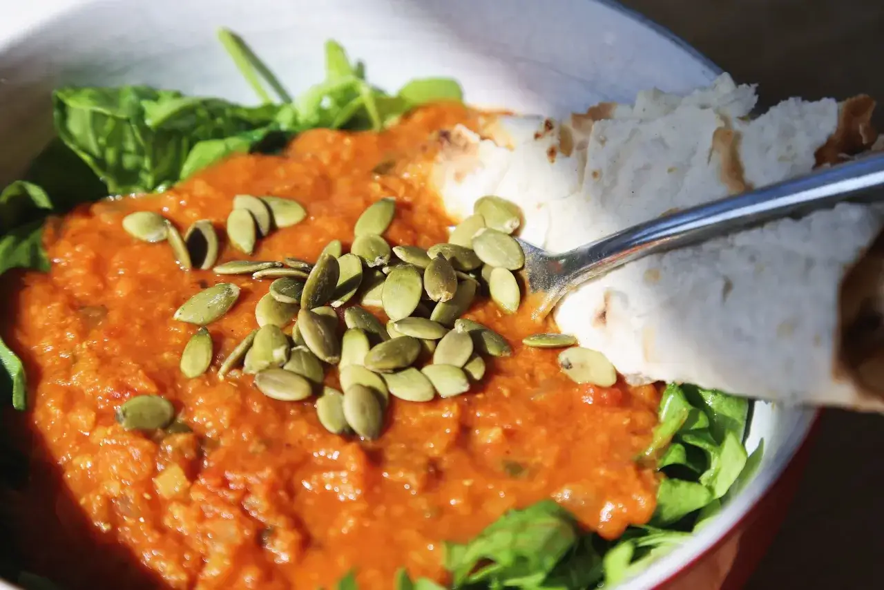 Schüssel mit Linsensuppe, Kürbiskernen und Fladenbrot. Informiere dich über die roten Linsen Nährwerte für eine gesunde Mahlzeit.