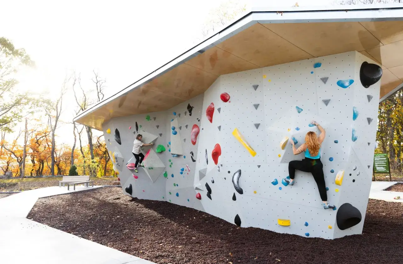 Bouldering co to? Dwie osoby wspinają się po ściankach wspinaczkowych na świeżym powietrzu, pokonując kolorowe chwyty.