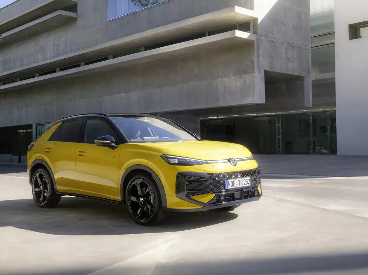 Gul Volkswagen T-Roc hybrid parkerad framf&ouml;r en modern betongbyggnad.