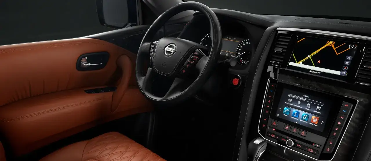 Wnętrze luksusowego **Nissan Patrol 2025** z brązową skórzaną tapicerką, multimedialnym ekranem nawigacji i przyciskiem start/stop.