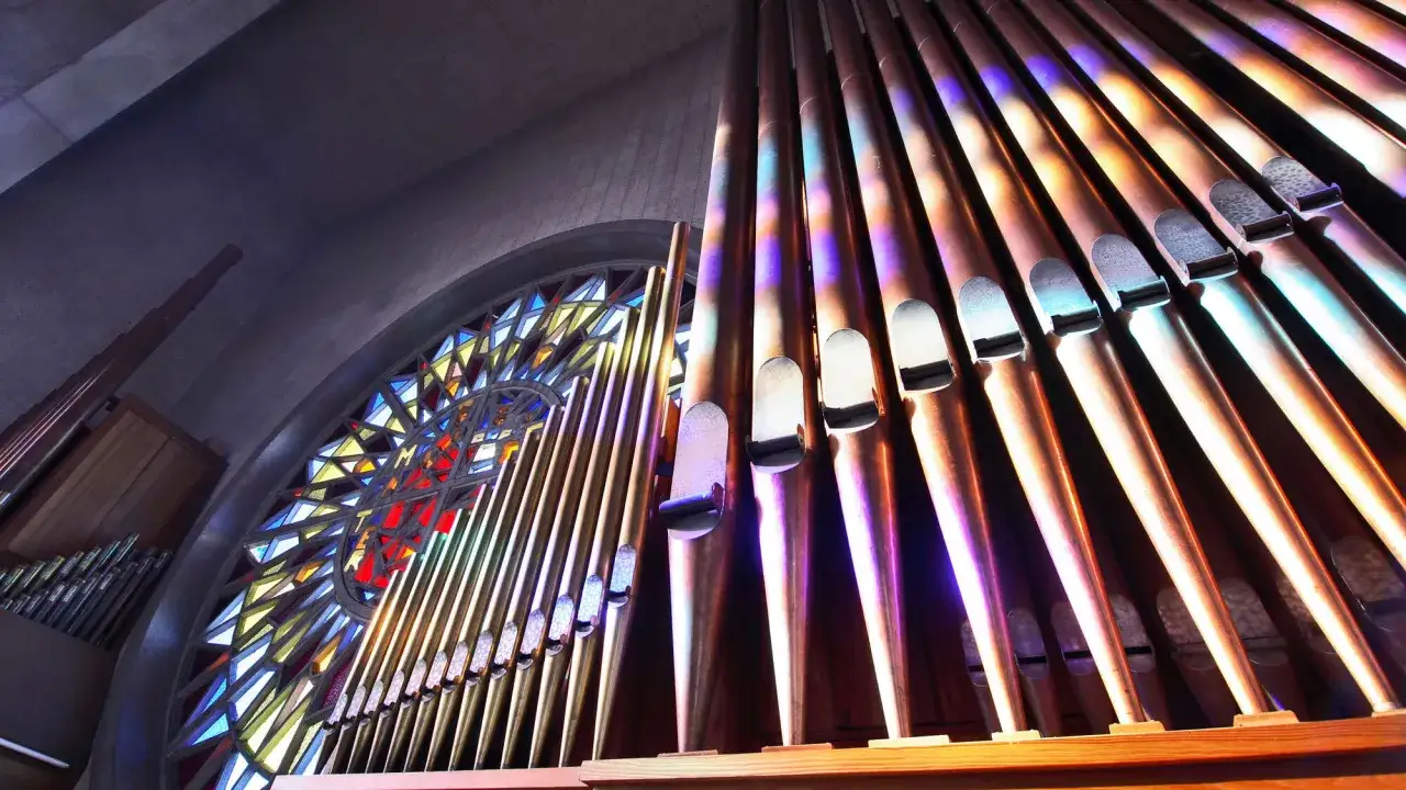Orgelpfeifen im Licht eines Buntglasfensters. Ein Ort, der nach kirchenmusik stellenangebote ruft.