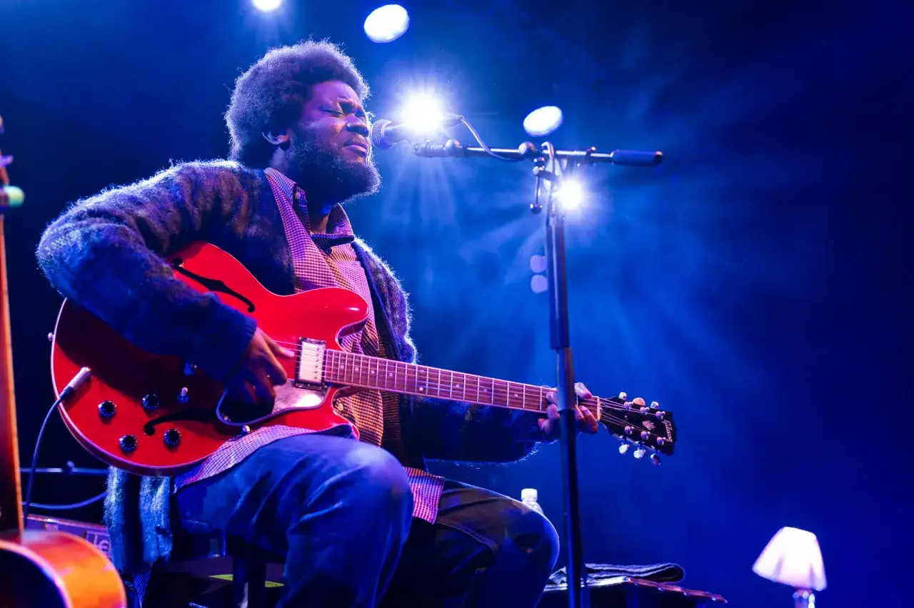 Michael Kiwanuka spielt leidenschaftlich seine rote E-Gitarre unter blauem B&uuml;hnenlicht.