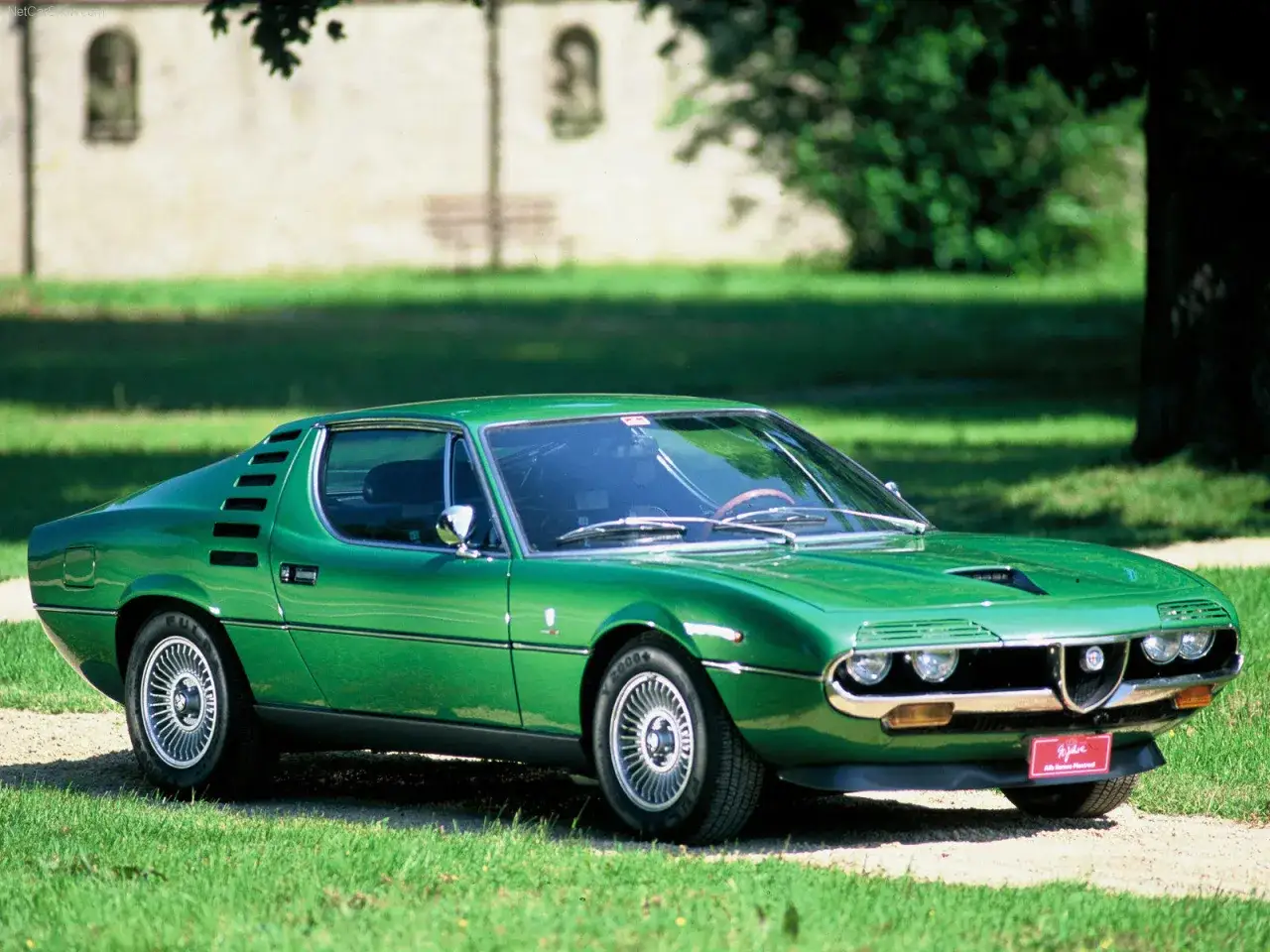 Zielona Alfa Romeo Montreal, jeden z ikonicznych modeli marki, prezentuje swoje sportowe linie na tle zieleni.