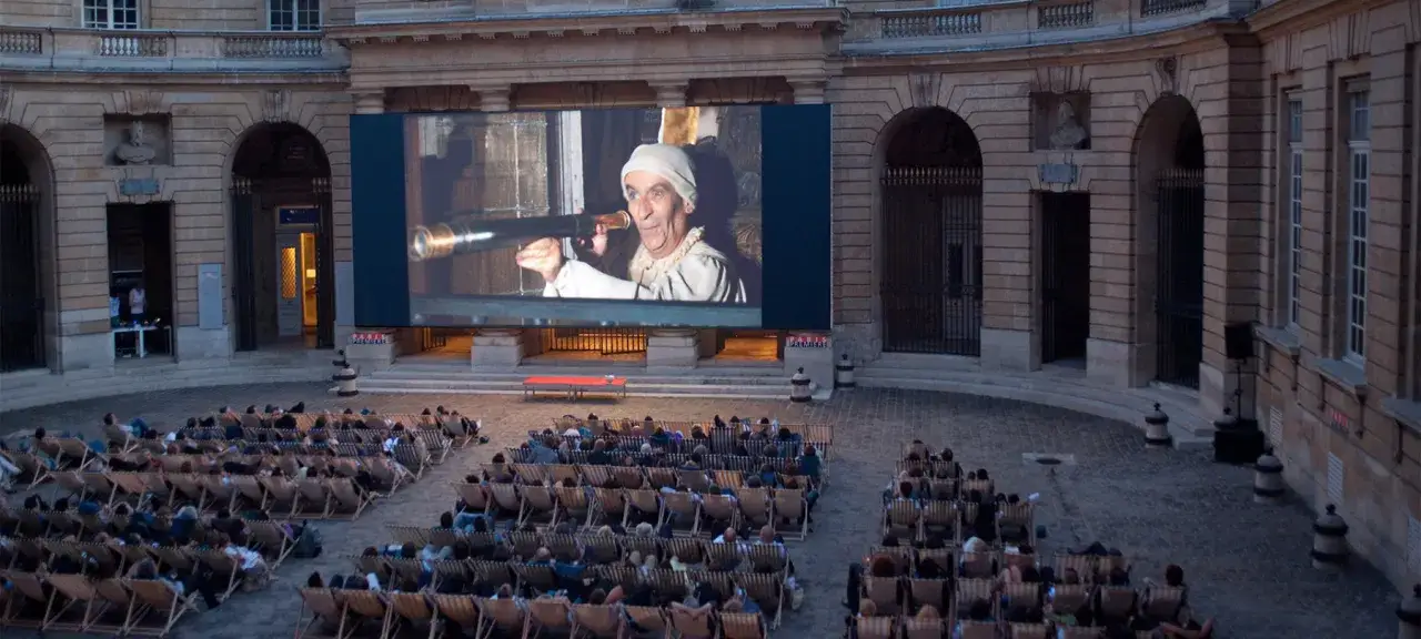 Un homme regarde dans une lunette sur un &eacute;cran g&eacute;ant, lors d'une soir&eacute;e cin&eacute;ma plein air.