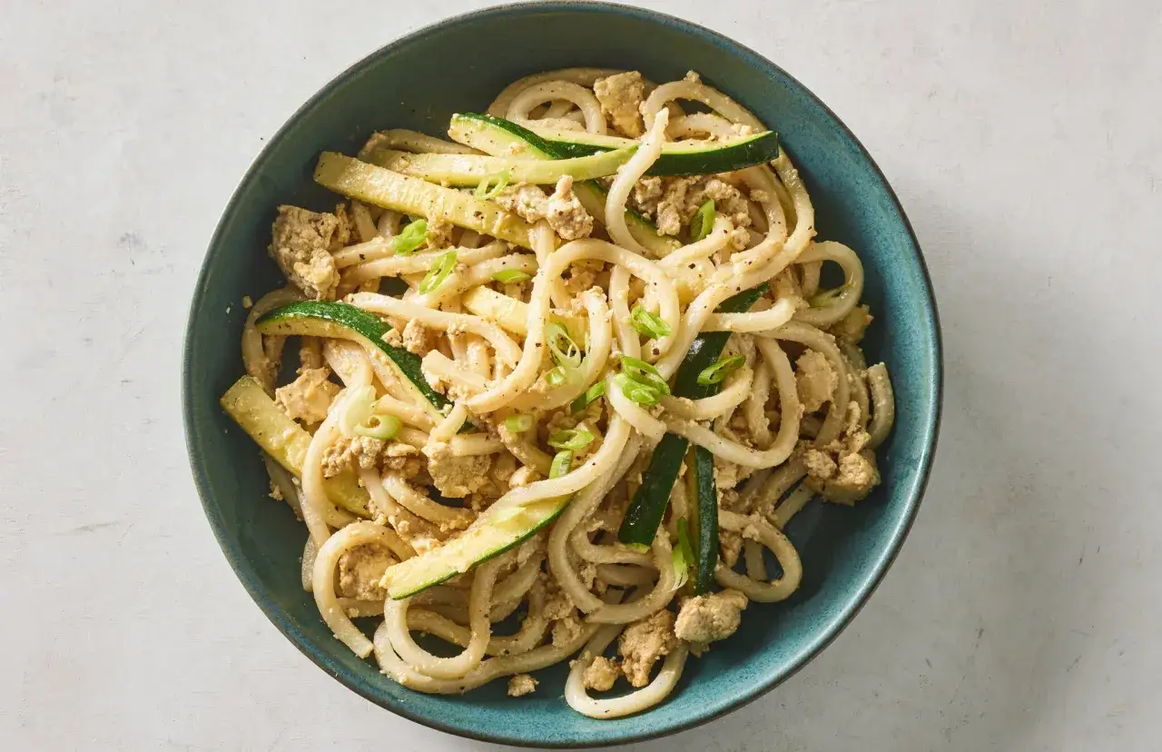 Udon z tofu i cukinią, posypane szczypiorkiem. Pyszne danie w niebieskiej misce.