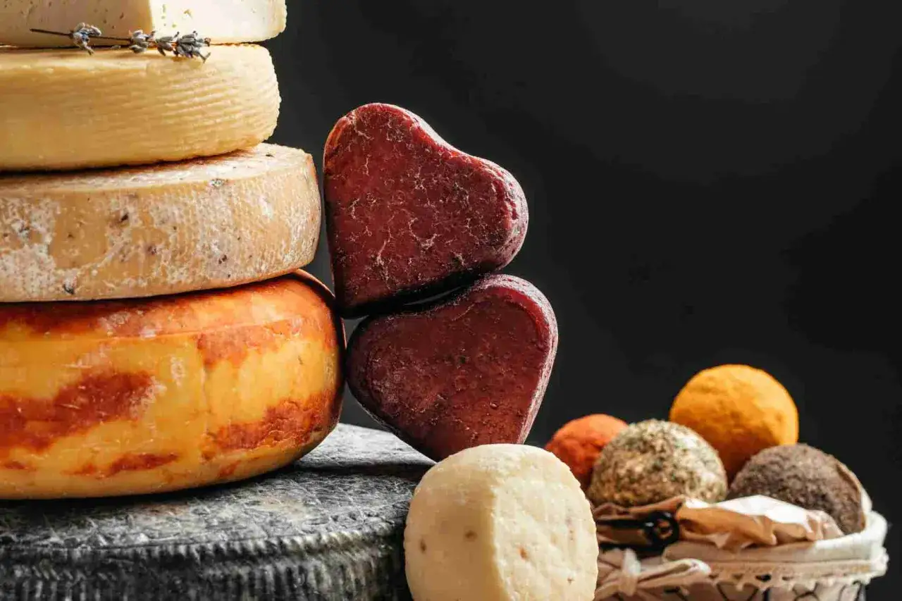 Varietà di formaggi a pasta cotta, tra cui forme a cuore rosse e rotonde in un cesto.
