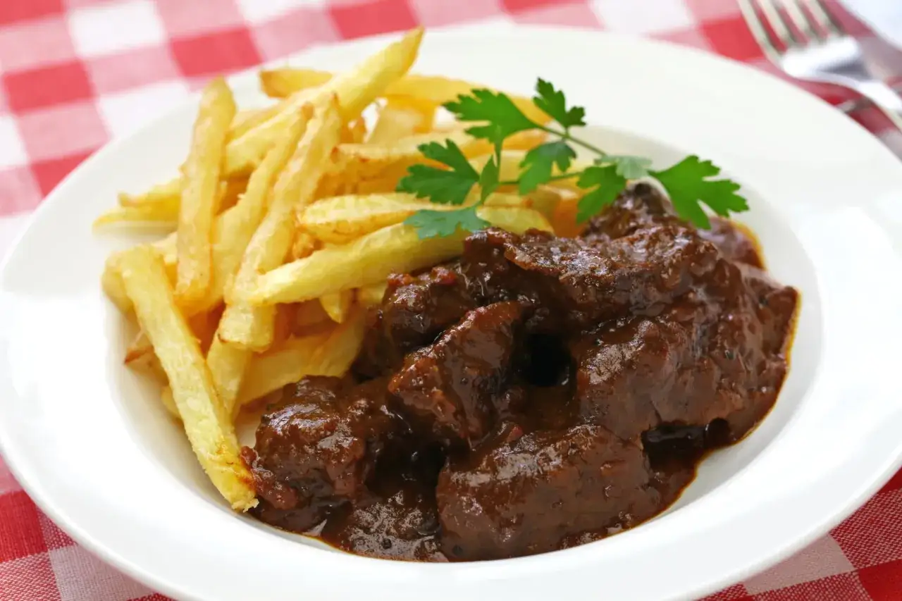 Une assiette de carbonade flamande, un plat mijot&eacute; de b&oelig;uf &agrave; la bi&egrave;re, servi avec des frites dor&eacute;es et une touche de persil frais.