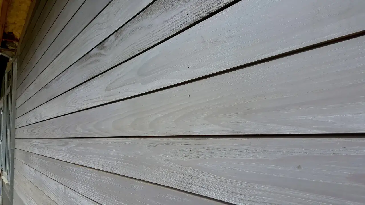 Bardage en bois gris clair, la peinture sur bois révèle les veines du bois.