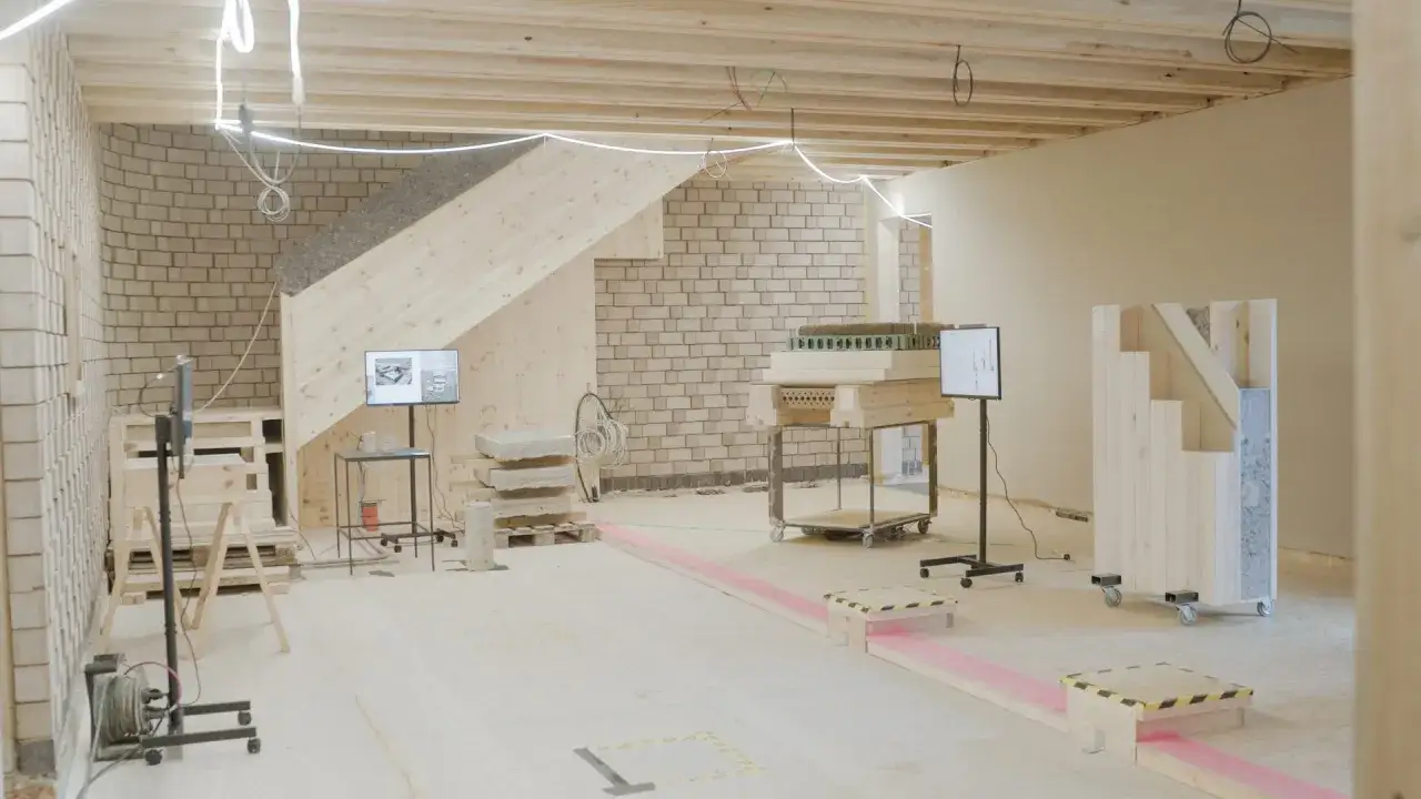 Ein Ausstellungsraum mit Holzkonstruktionen, Ziegelwänden und Bildschirmen, die nachhaltige Materialien zeigen.