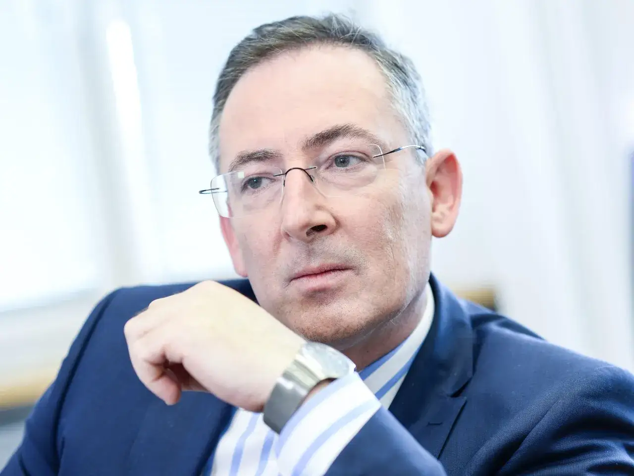 Poseł Bartłomiej Sienkiewicz w okularach, w granatowej marynarce i pasiastym krawacie, z ręką opartą na brodzie.
