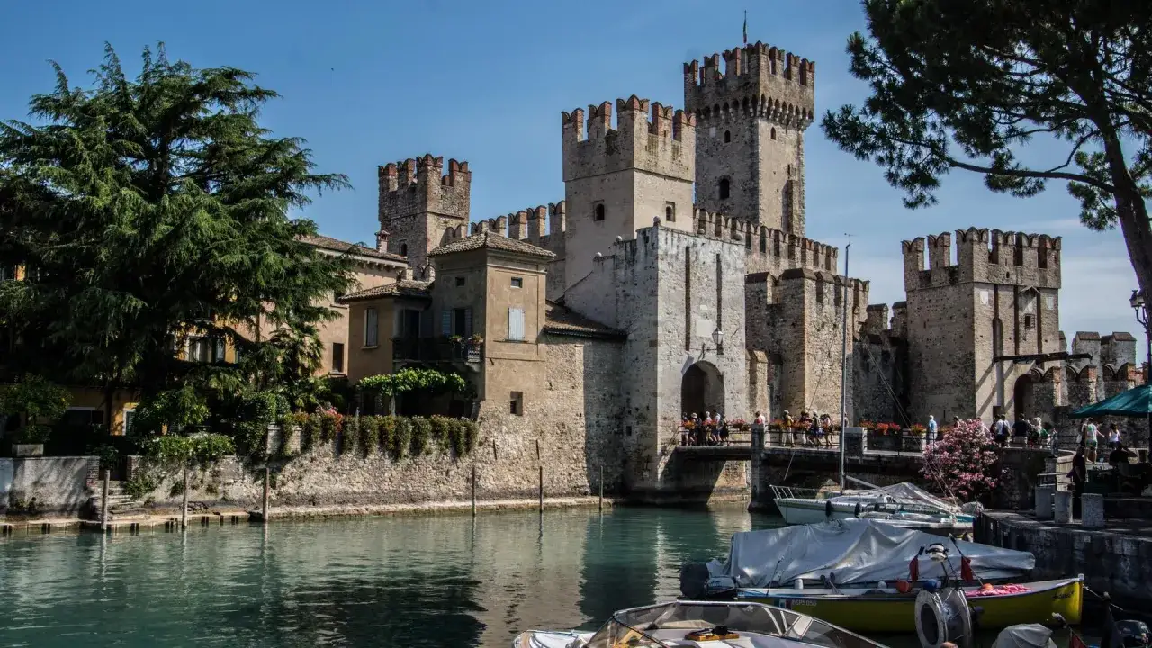 Antico castello sul lago, uno dei magnifici castelli lombardia, con barche ormeggiate e gente che passeggia.