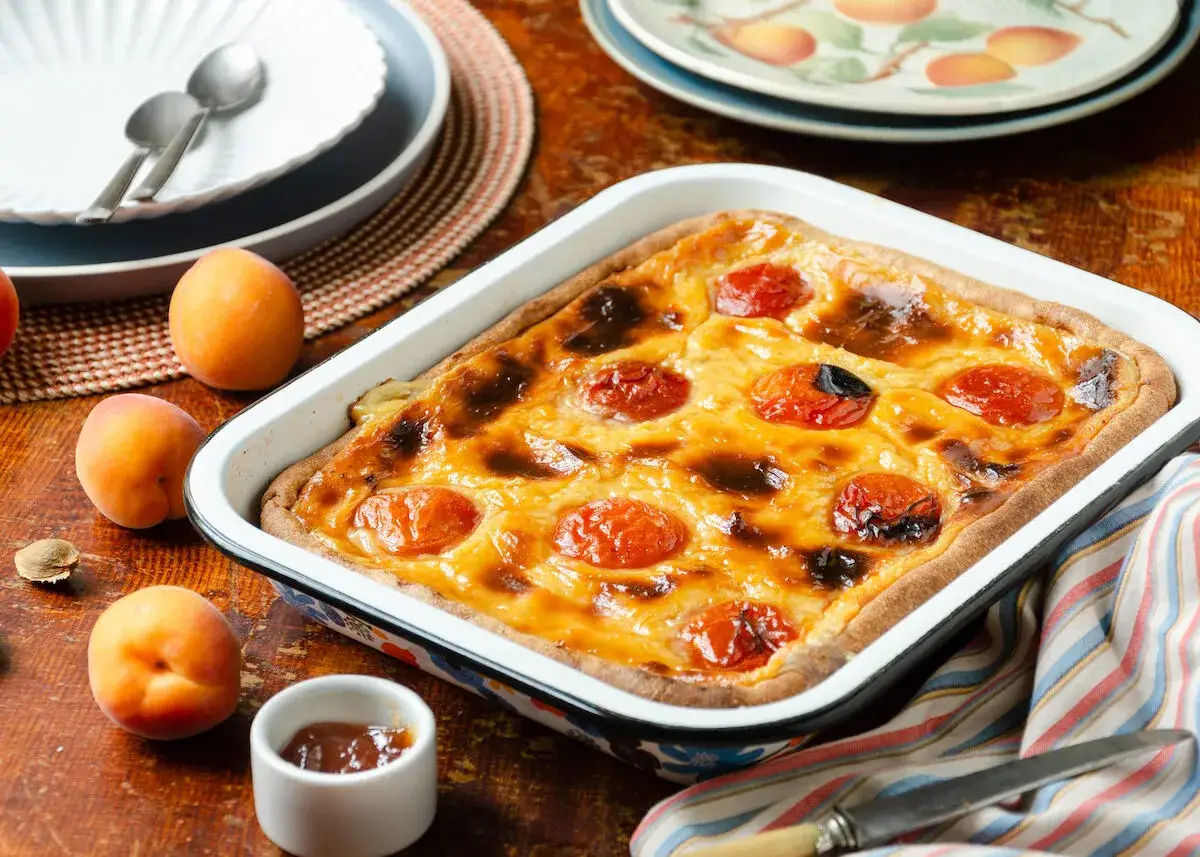 Un délicieux flan aux abricots tout juste sorti du four, avec des fruits frais et une touche de confiture sur le côté.