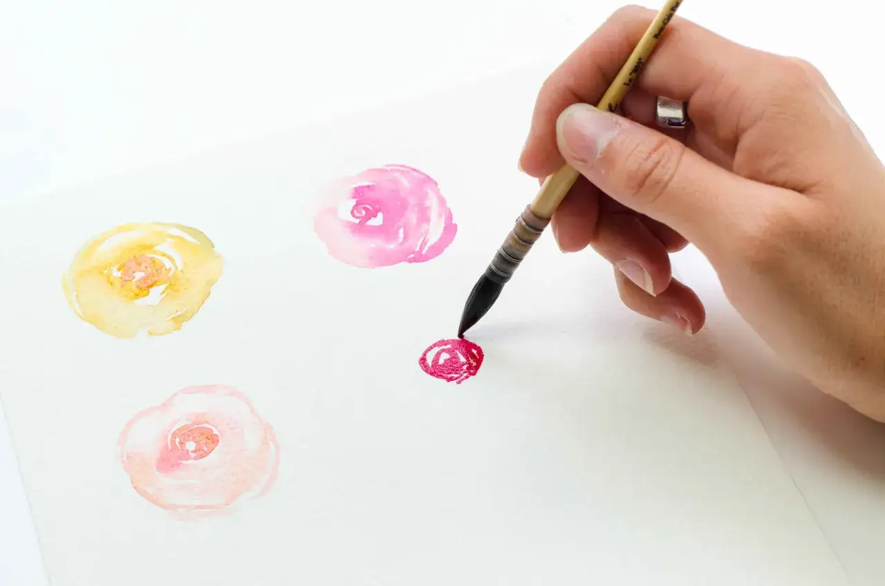 Une main peint des fleurs à l'aquarelle. Un bouquet de fleurs peinture facile prend forme sur le papier blanc.