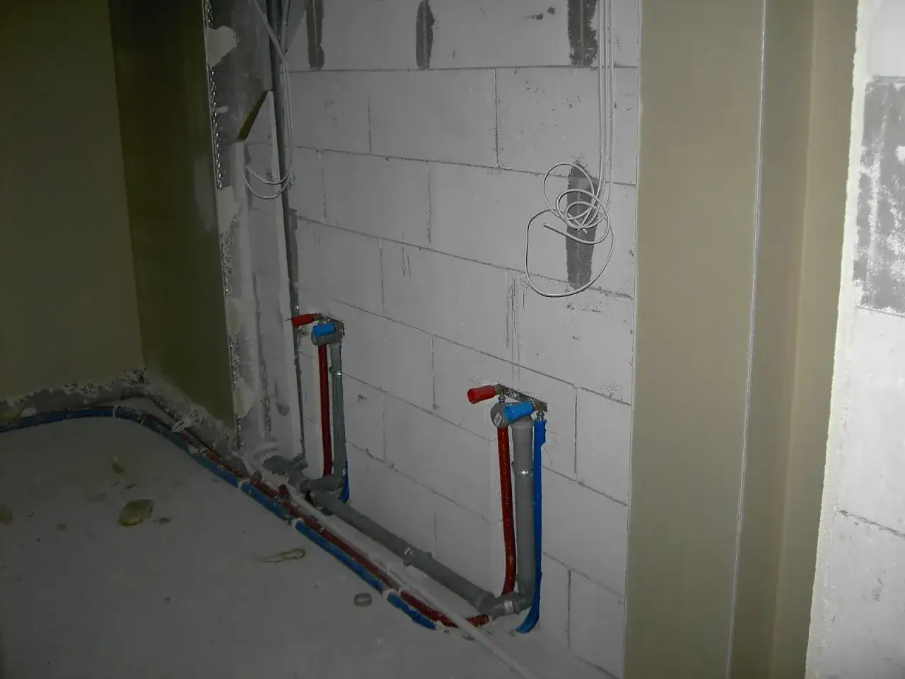 Instalacja hydrauliczna przed tynkami: widoczne rury wodne i kanalizacyjne na ścianie z bloczków, gotowe do ukrycia.