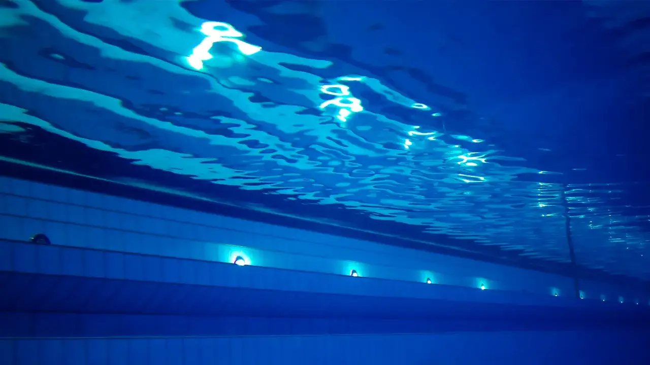 Podwodny widok na basen sportowy Term Maltańskich. Błękitna woda, falująca powierzchnia i światła podwodne tworzą spokojną atmosferę.