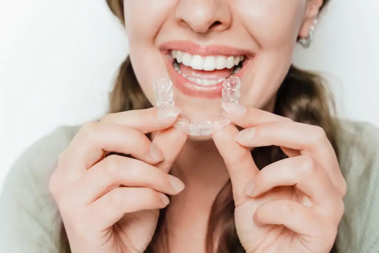 Uśmiechnięta kobieta trzyma przezroczysty aparat Invisalign, gotowa do prostowania zębów.