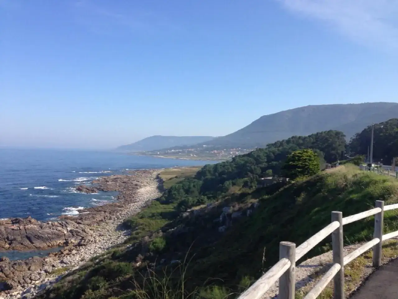 Costa rocosa y mar azul en A Guarda, Baiona. Montañas verdes y cielo despejado.