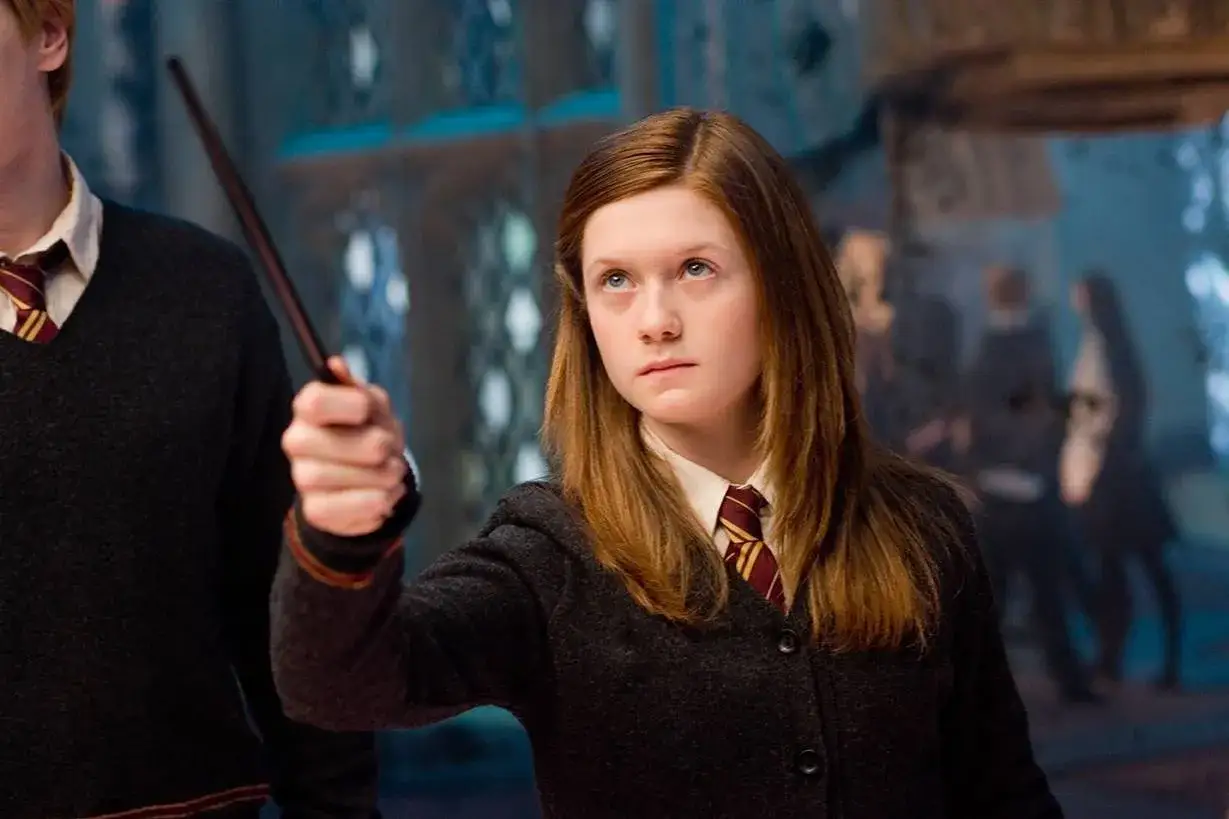 Bonnie Wright jako Ginny Weasley w filmach o Harrym Potterze, trzymająca różdżkę.